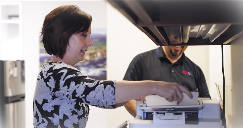 Office worker and technician reviewing documents on a multi-function printer.