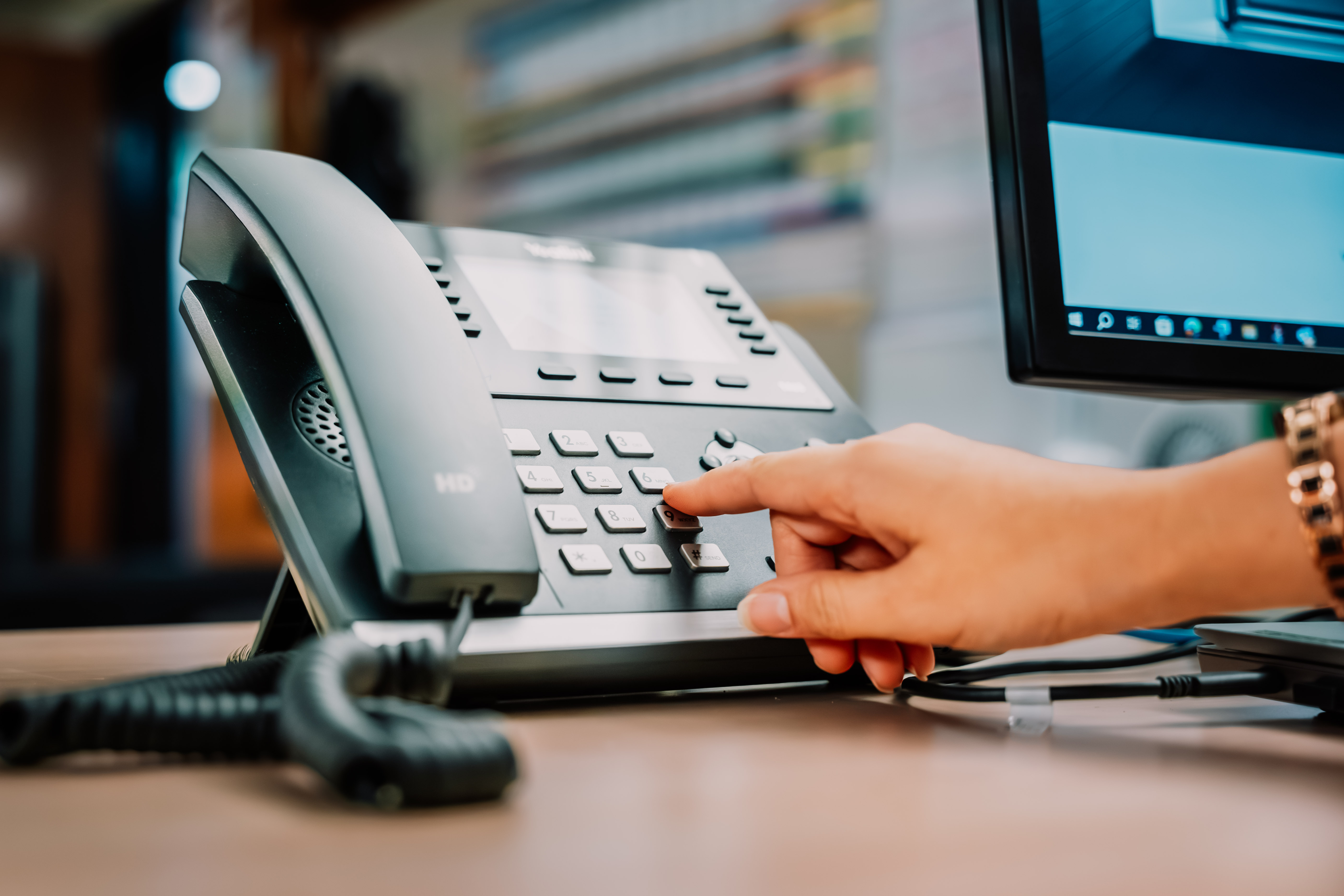 A hand dials the keypad of a desk phone